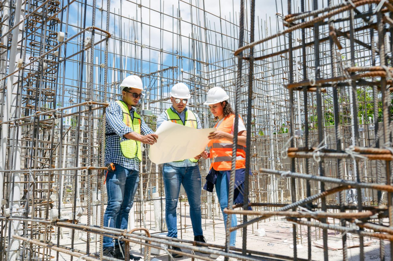 Three workers discuss building plans on a construction site