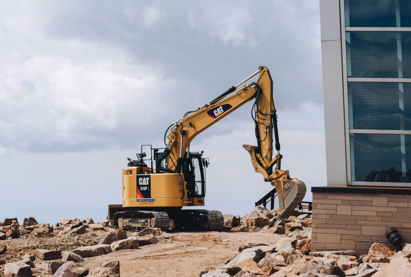 An image of an excavator surrounded by rocks outside of a building