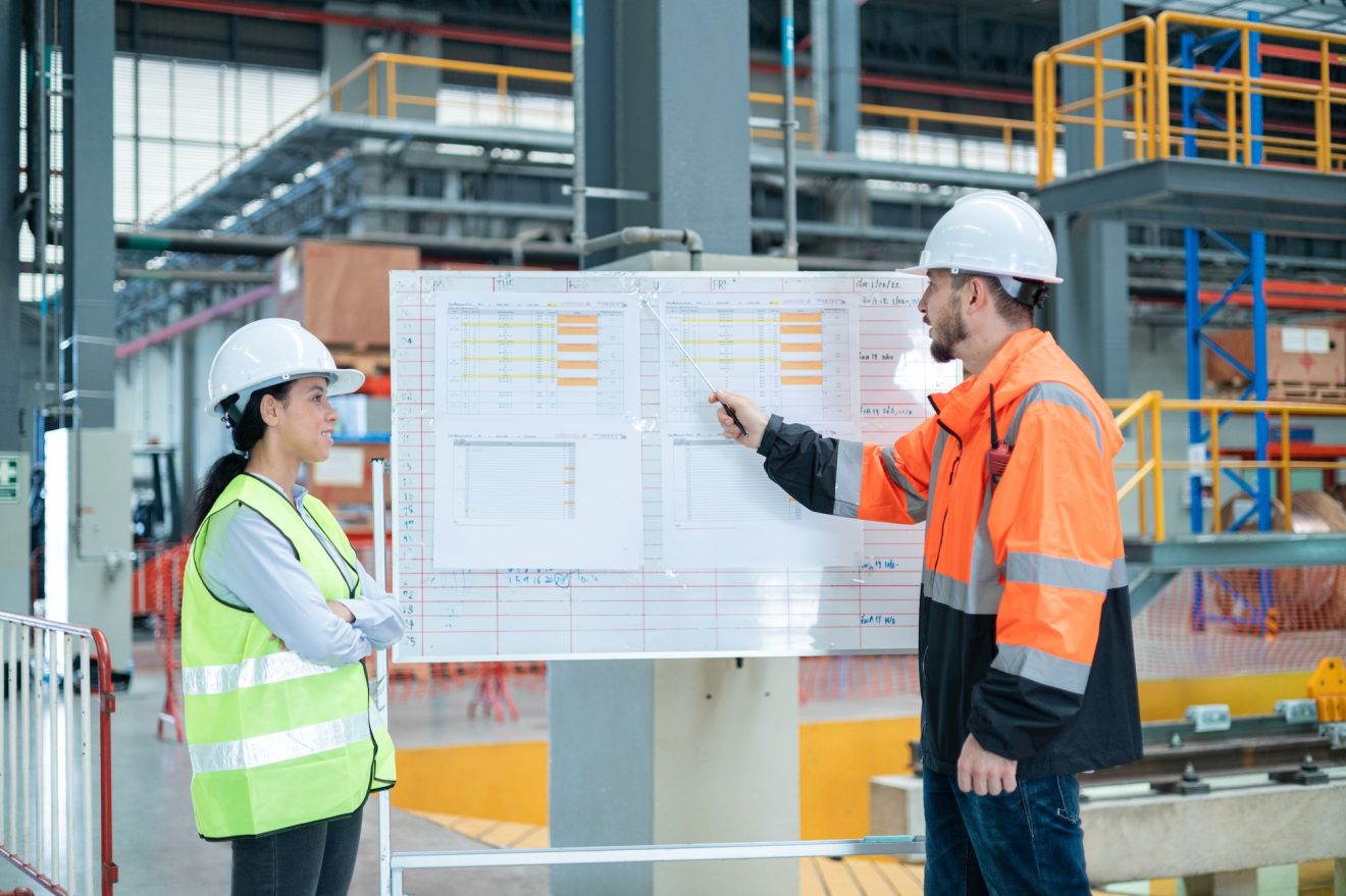 Two construction workers look at a project whiteboard