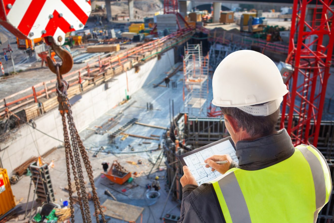 Person in hardhat and safety vest using a tablet while on a construction site
