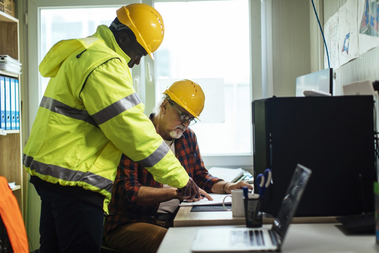 Two men in hardhats reviewing construction plans at a desk
