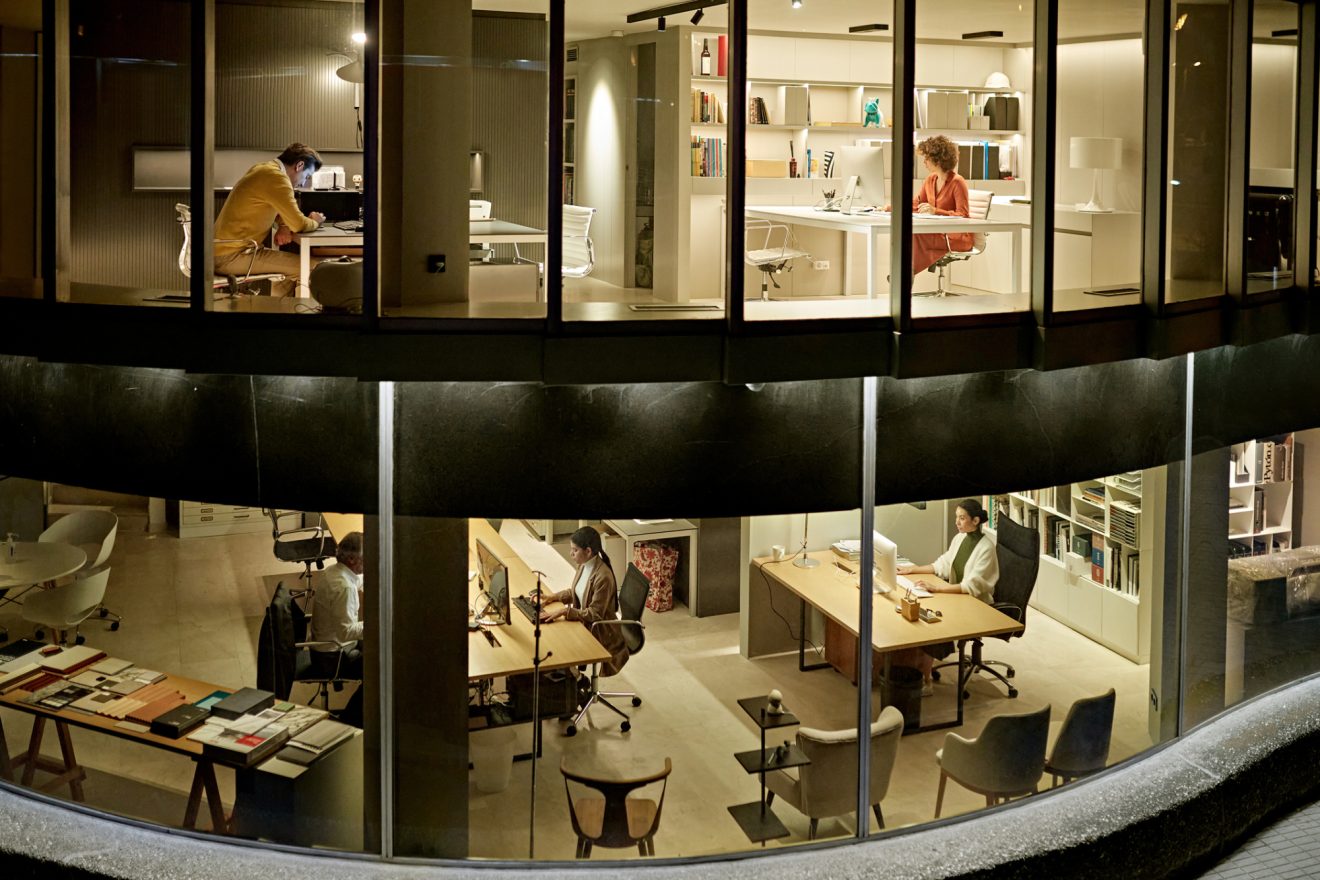 Exterior shot of an office building at night with lights on and people working at their desks