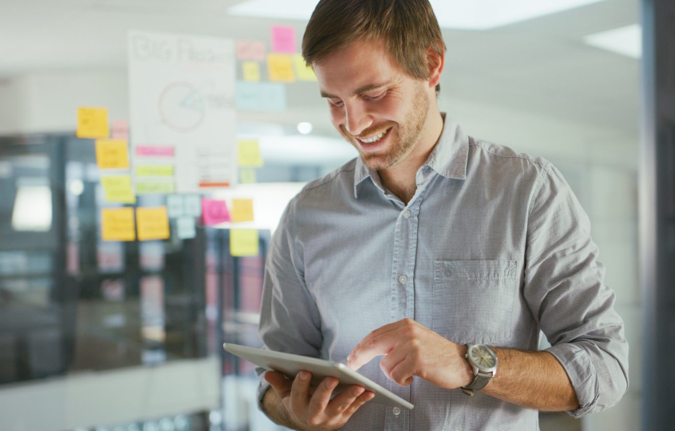 Man in office smiling while using a tablet