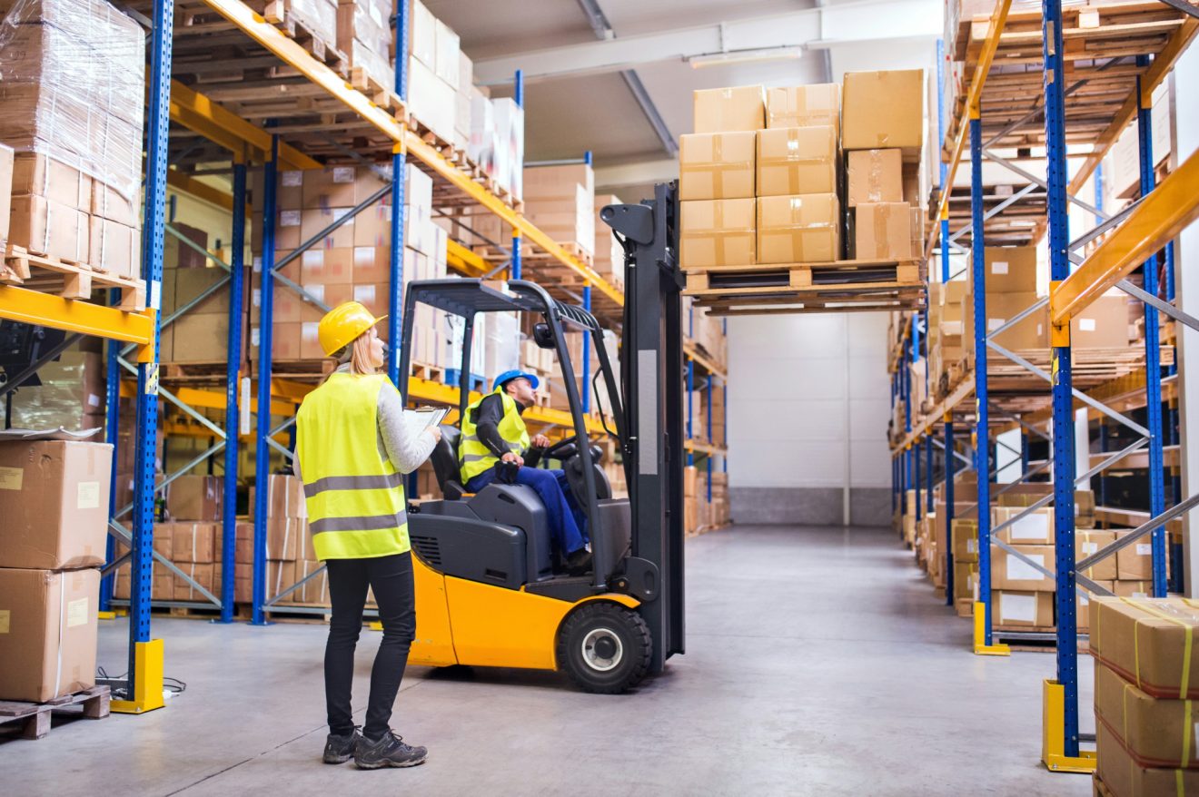 Two people are collaborating in a warehouse, one on a forklift and the other on a tablet