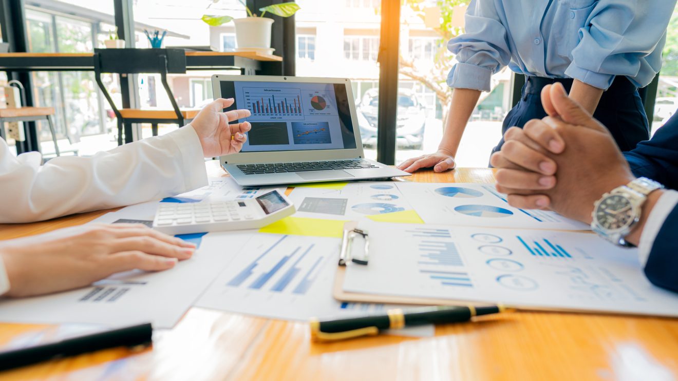 A group of people reviewing a business presentation at a desk with graphs and charts on it