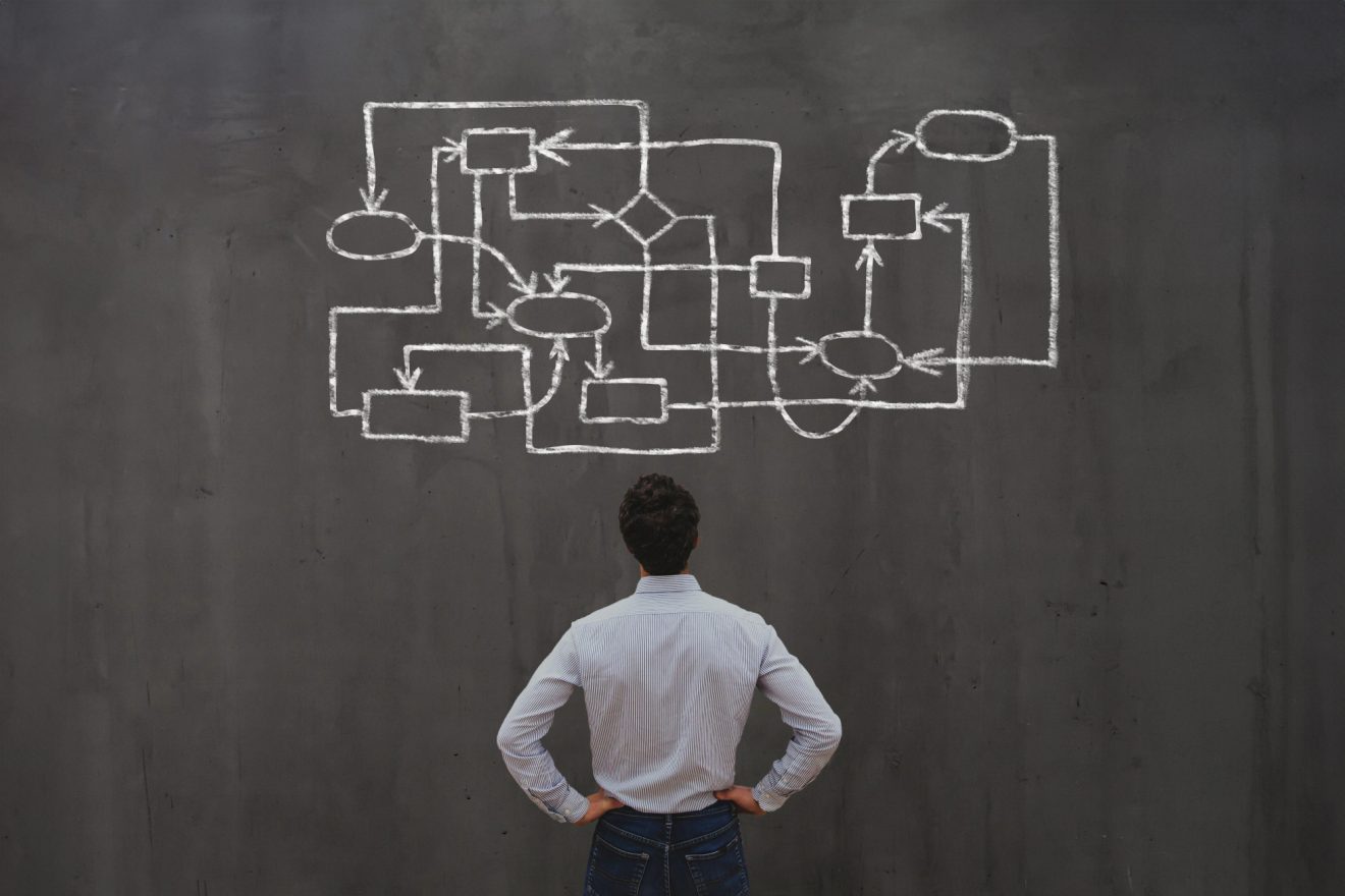 Man standing in front of a process workflow diagram on a chalkboard