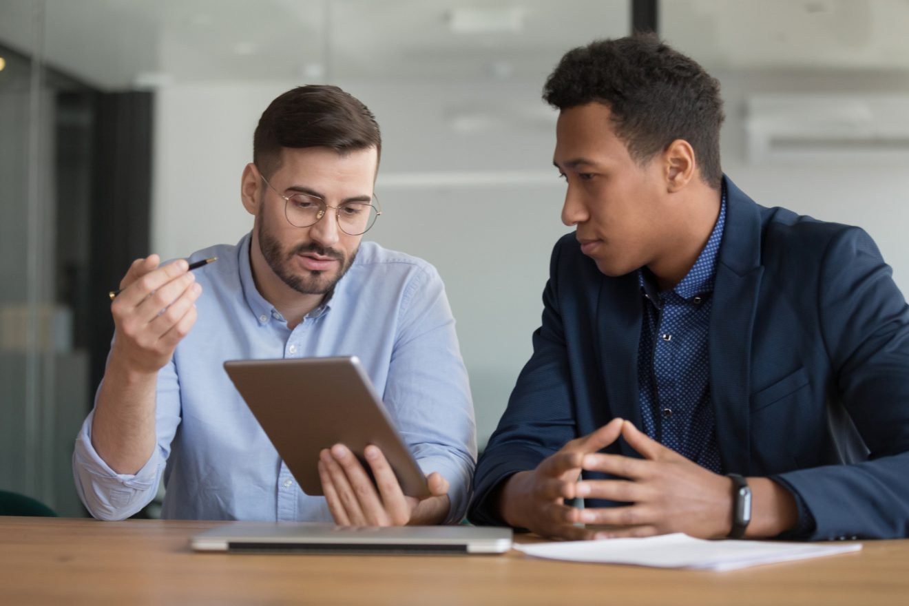 Two male coworkers working on project using tablet discuss online apps