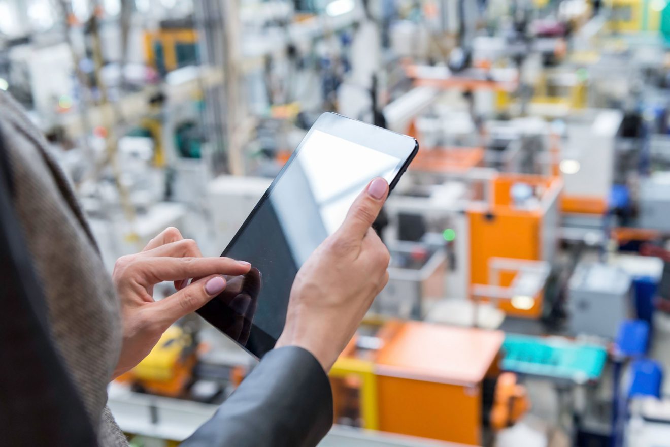 A person touching a tablet screen while overlooking a warehouse floor.