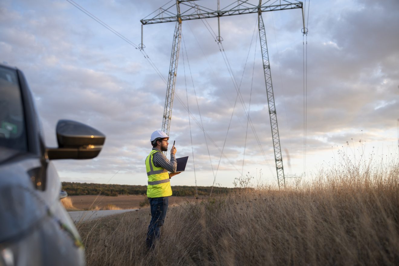 A man surveys a cell tower with a tablet in his hand