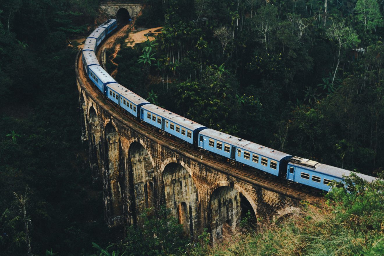 A blue train crosses an old bridge