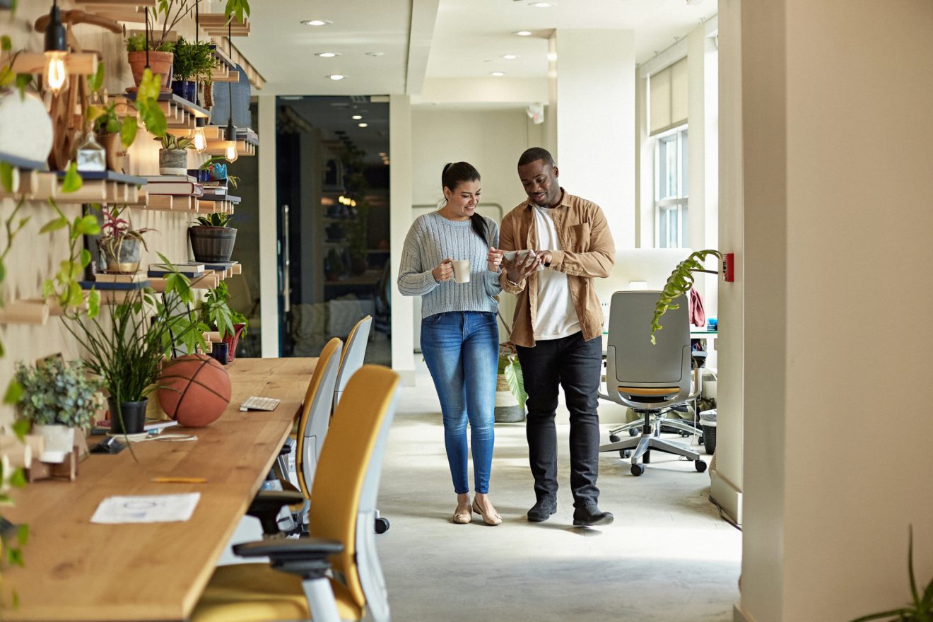 Two people talk as they walk through an office hallway