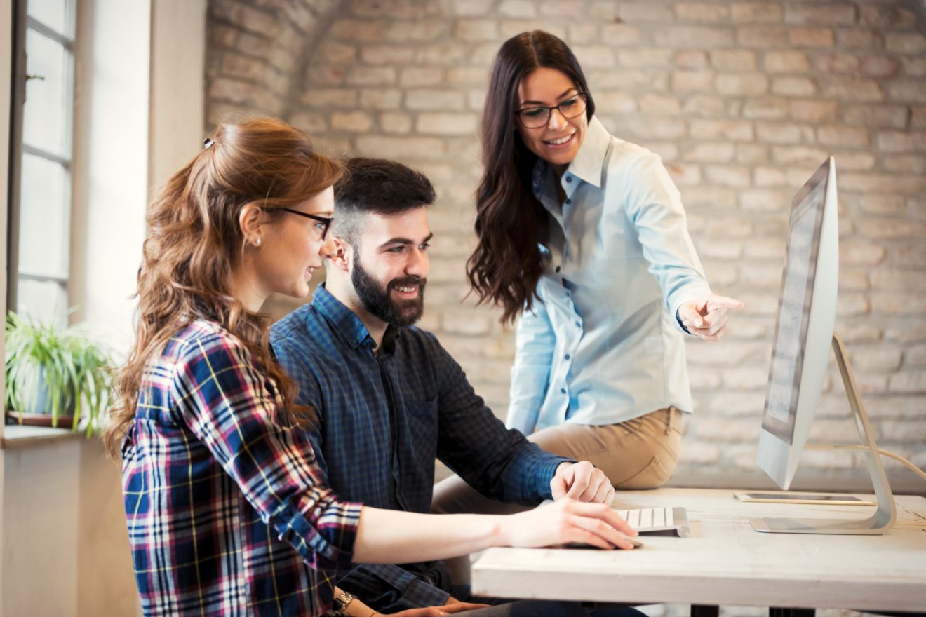 Three people discuss a project, displayed on a desktop computer