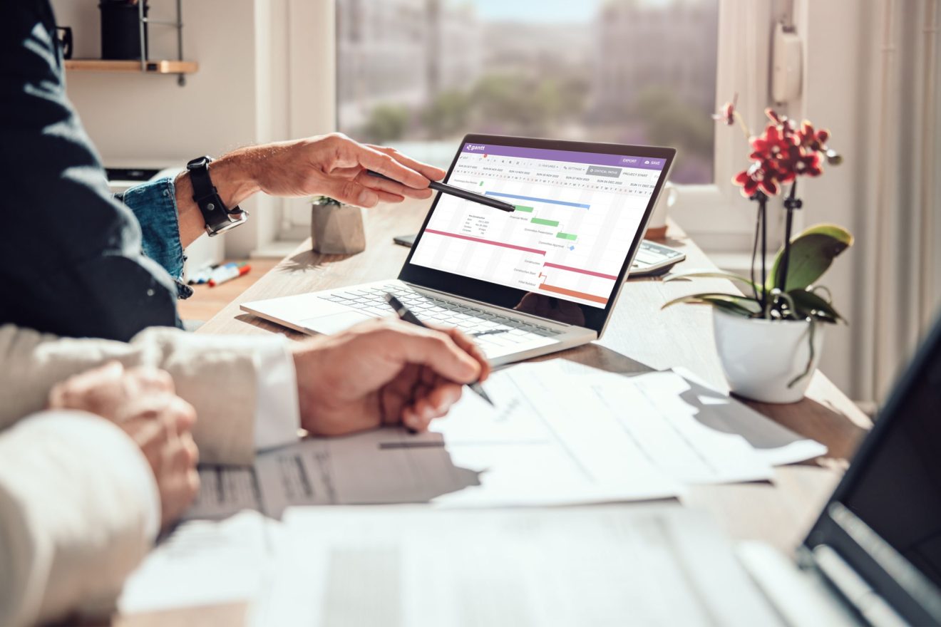 Two people reference a laptop with a Quickbase Gantt chart open