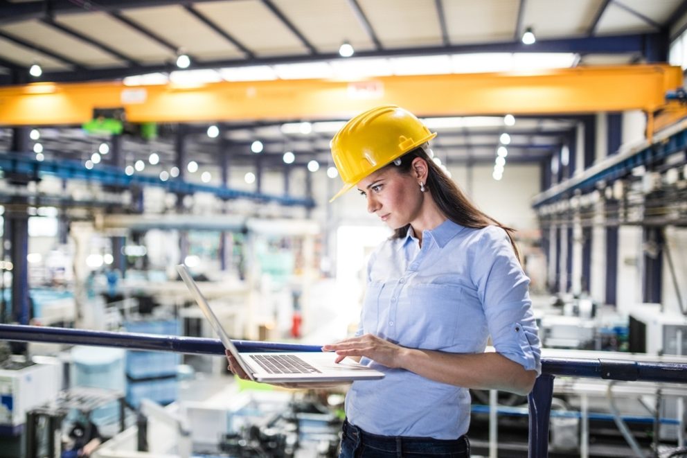 Project manager standing in modern industrial factory holding a laptop