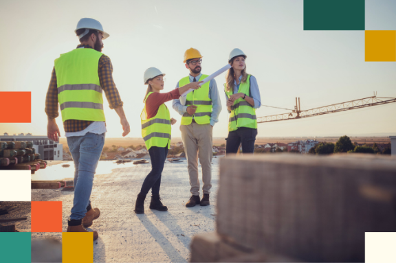 female construction site manager in hard hat and reflective vest holding blueprint and pointing in distance surrounded by two male and one female construction worker
