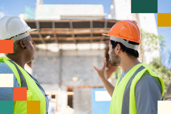 man and woman in hard hats and reflective vests looking at partially built buillding