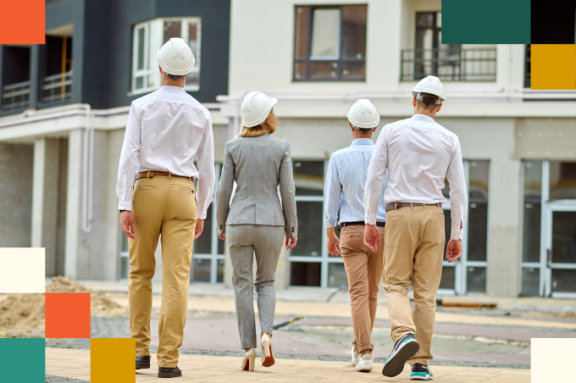 small group of men and women in business attire wearing hard hats walking through nearly complete construction project
