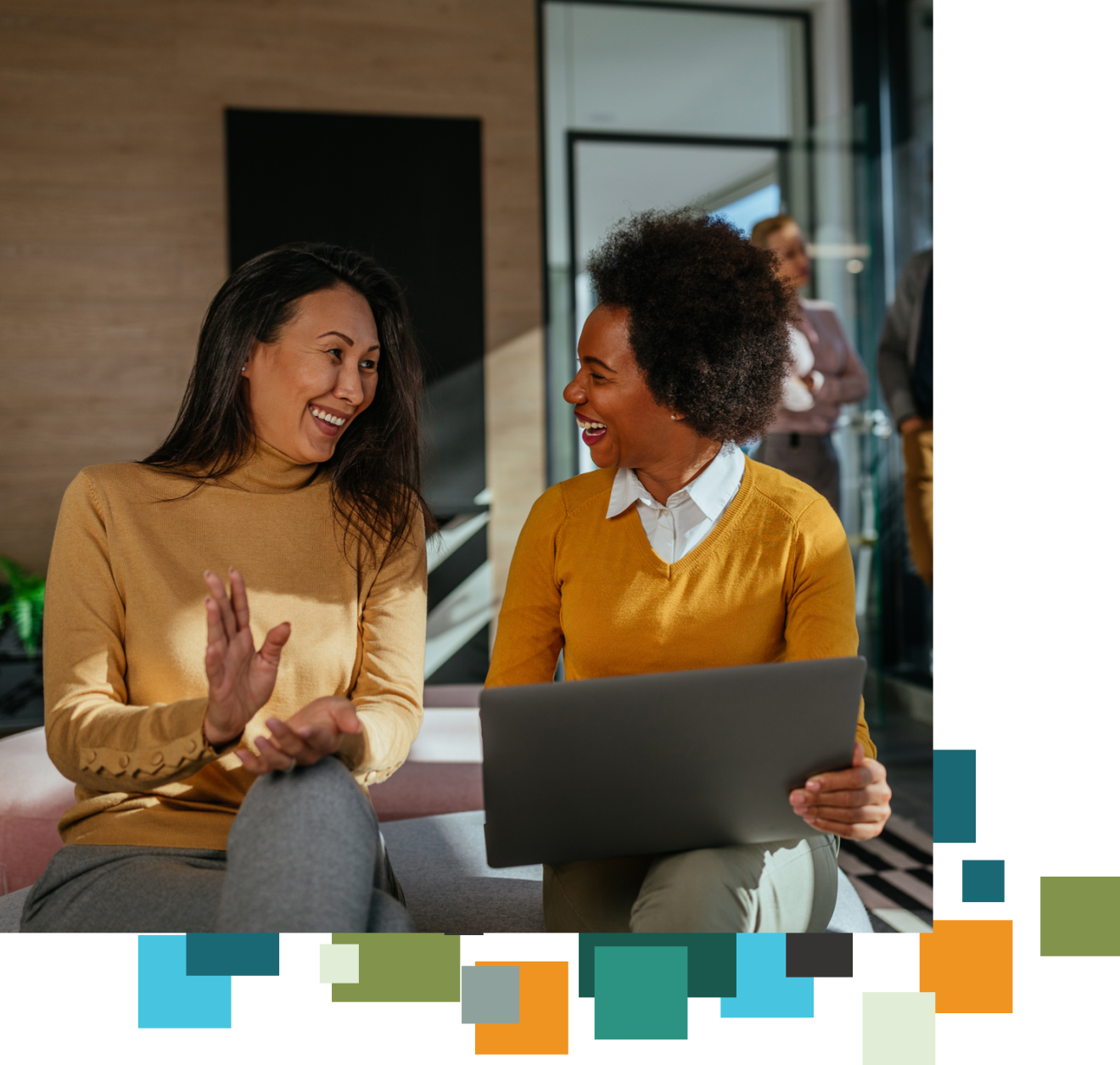 An image of two women laughing together. One holds a laptop.
