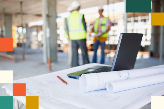 Construction workers behind blueprints and laptop on construction site